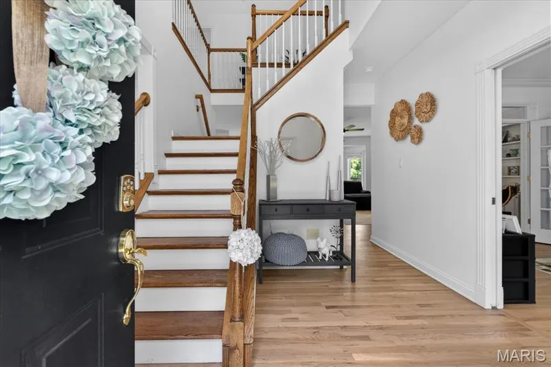 Open entryway with a dark paneled door featuring brass hardware, wood-finish flooring, a wood staircase with white risers and spindles, and a recessed doorway — 17821 Wilderness Cliff Court, Wildwood, MO 63005