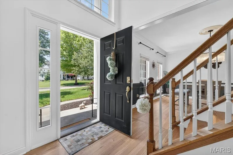 Entryway featuring a dark paneled door, sidelight windows, a transom window, wood-finish flooring, and a hardwood staircase with white balusters — 17821 Wilderness Cliff Court, Wildwood, MO 63005