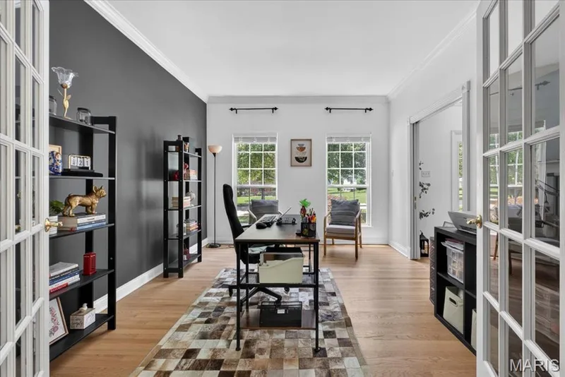 French doors opening to a versatile interior space featuring wood-finish flooring, a contrasting accent wall, and crown molding — 17821 Wilderness Cliff Court, Wildwood, MO 63005