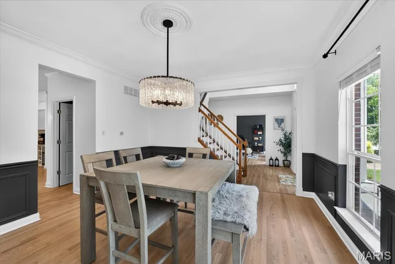Dining area featuring hardwood flooring, wainscoting, an ornate ceiling medallion, a modern chandelier, and a large window with white trim — 17821 Wilderness Cliff Court, Wildwood, MO 63005
