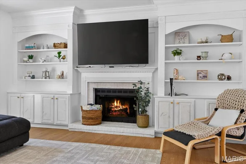 Central fireplace featuring a stone hearth and surround, flanked by custom built-in cabinetry with arched open shelving and lower storage — 17821 Wilderness Cliff Court, Wildwood, MO 63005
