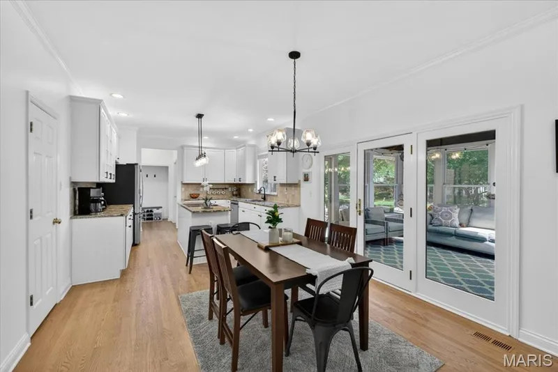 Open-concept kitchen and dining area featuring wood-finish flooring, white cabinetry, a kitchen island with seating, a tile backsplash, and recessed lighting — 17821 Wilderness Cliff Court, Wildwood, MO 63005
