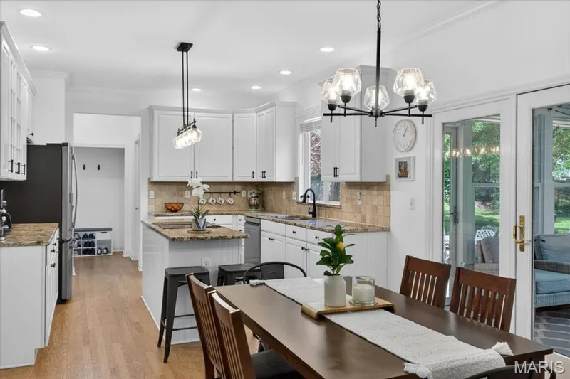 Kitchen and dining area featuring white cabinetry, granite countertops, tile backsplash, and wood-finish flooring — 17821 Wilderness Cliff Court, Wildwood, MO 63005