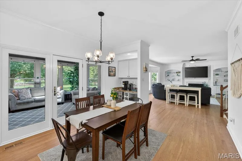 Dining area featuring a contemporary chandelier, wood-finish flooring, white trim, and double glass-paneled doors opening to an enclosed patio — 17821 Wilderness Cliff Court, Wildwood, MO 63005