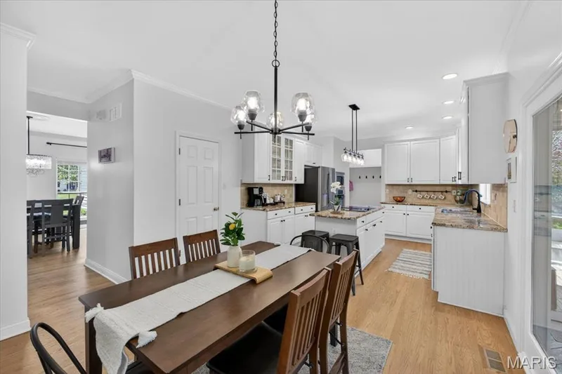 Open-concept dining area featuring a dark wood-finish table, wood-finish flooring, and a contemporary chandelier — 17821 Wilderness Cliff Court, Wildwood, MO 63005