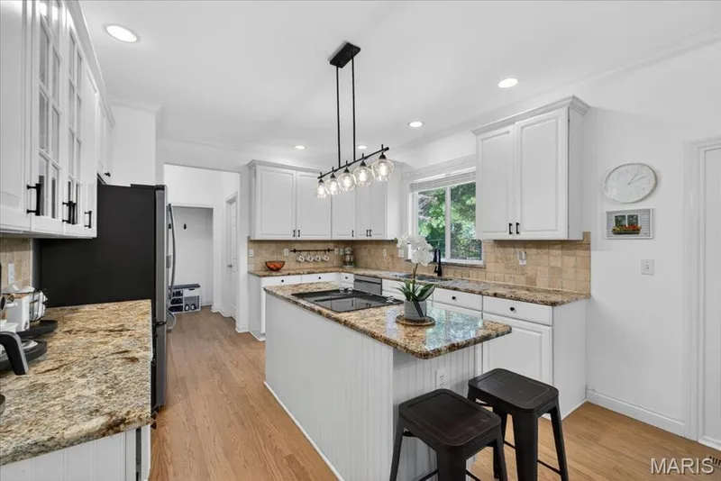 Kitchen featuring an island with beadboard paneling, recessed lighting, wood-finish flooring, a tile backsplash, and white cabinetry with dark hardware — 17821 Wilderness Cliff Court, Wildwood, MO 63005