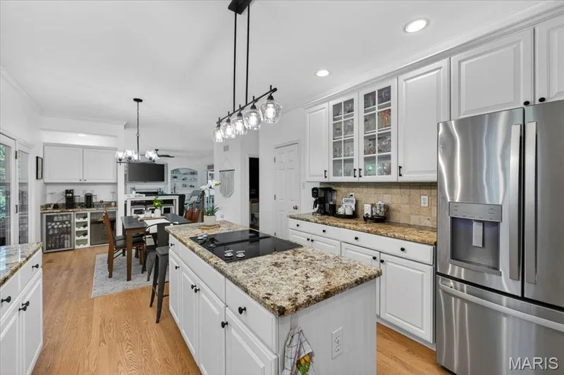 Well-appointed kitchen featuring a center island cooktop, stainless steel appliances, white cabinetry, and granite countertops — 17821 Wilderness Cliff Court, Wildwood, MO 63005