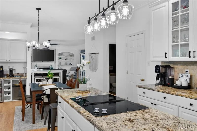 Kitchen featuring a spacious island with an integrated cooktop, stone countertops, white cabinetry with dark hardware, and a tile backsplash — 17821 Wilderness Cliff Court, Wildwood, MO 63005