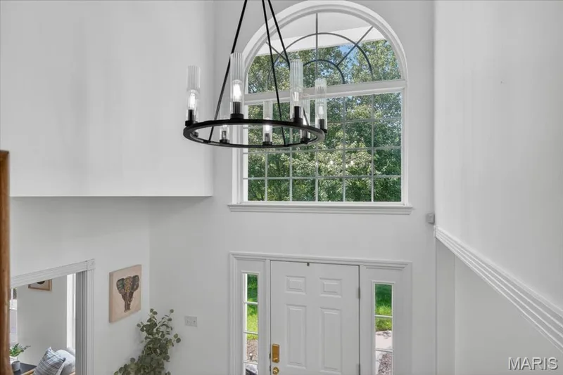 Two-story foyer featuring an arched transom window, a white paneled front door with sidelights, a contemporary circular chandelier, and white wall trim details — 17821 Wilderness Cliff Court, Wildwood, MO 63005