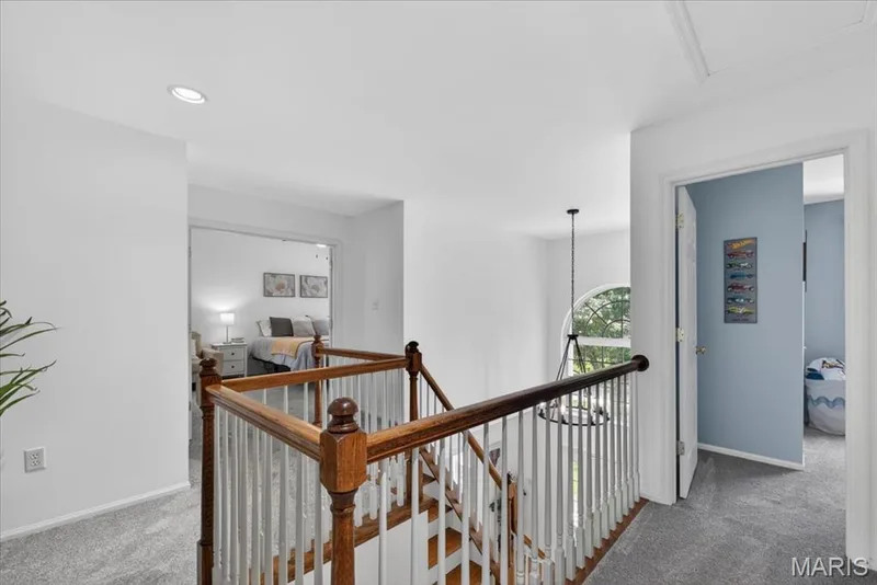 Upper-level landing featuring hardwood stair treads, a white spindle railing with wood handrails, and neutral carpeting — 17821 Wilderness Cliff Court, Wildwood, MO 63005