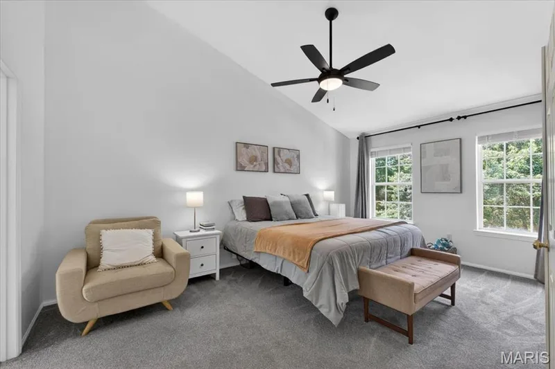 Spacious room featuring vaulted ceilings, a ceiling fan with integrated lighting, two large windows, and neutral carpeting — 17821 Wilderness Cliff Court, Wildwood, MO 63005