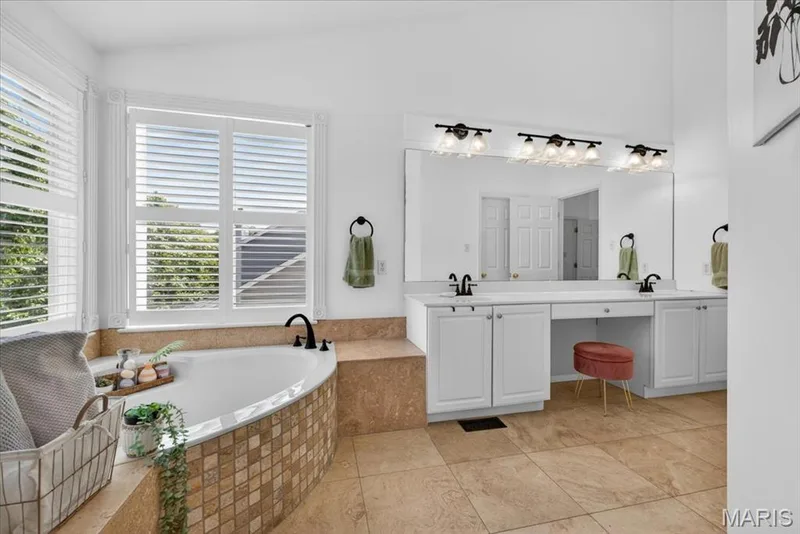 Bathroom featuring a corner soaking tub with tile surround, dual vanity with white cabinetry, integrated makeup area, and wood-finish flooring — 17821 Wilderness Cliff Court, Wildwood, MO 63005