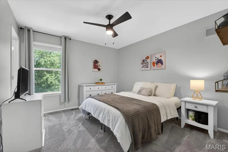 Bedroom featuring light gray walls, gray patterned carpeting, and a ceiling fan with integrated lighting — 17821 Wilderness Cliff Court, Wildwood, MO 63005