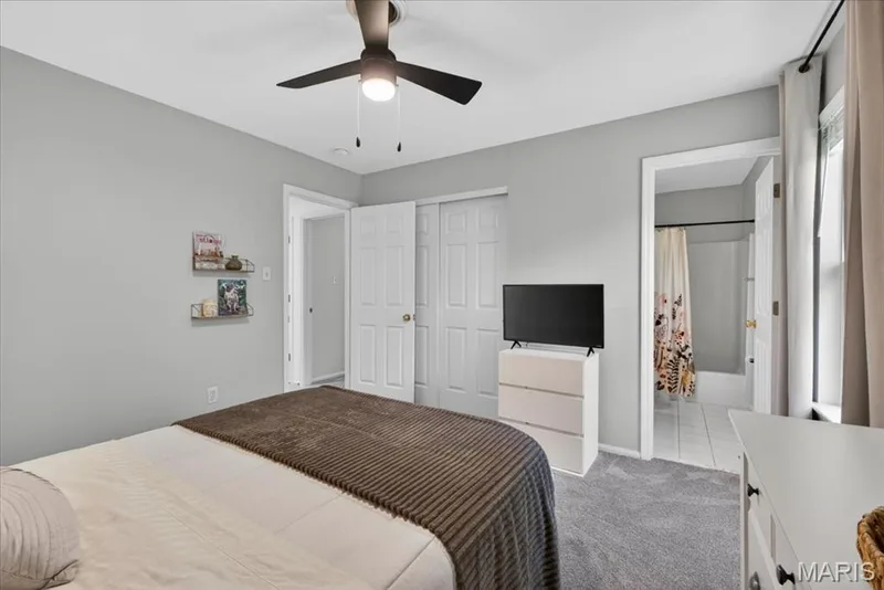 Light gray walls complement the gray carpeting in this bedroom featuring a ceiling fan with integrated lighting — 17821 Wilderness Cliff Court, Wildwood, MO 63005