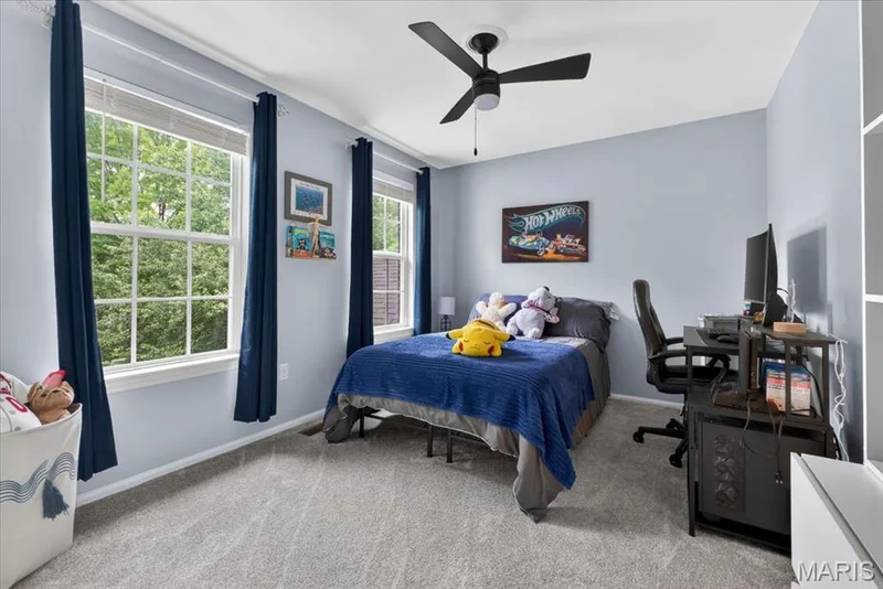 Room featuring two large windows, light blue wall paint, gray carpet flooring, a black ceiling fan, and built-in shelving — 17821 Wilderness Cliff Court, Wildwood, MO 63005