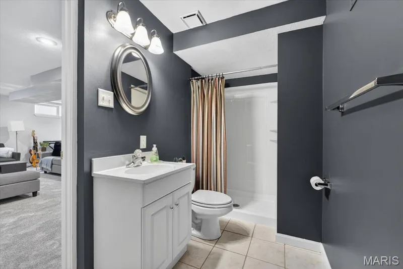 Bathroom featuring a white vanity with integrated sink, chrome faucet, oval mirror, and three-light vanity fixture — 17821 Wilderness Cliff Court, Wildwood, MO 63005