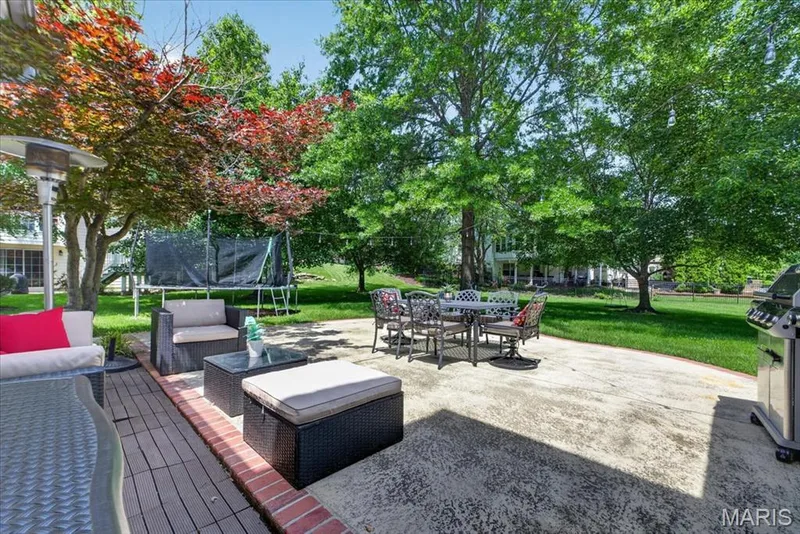 Expansive concrete patio with an adjacent wood-look deck, surrounded by mature trees and manicured lawn — 17821 Wilderness Cliff Court, Wildwood, MO 63005