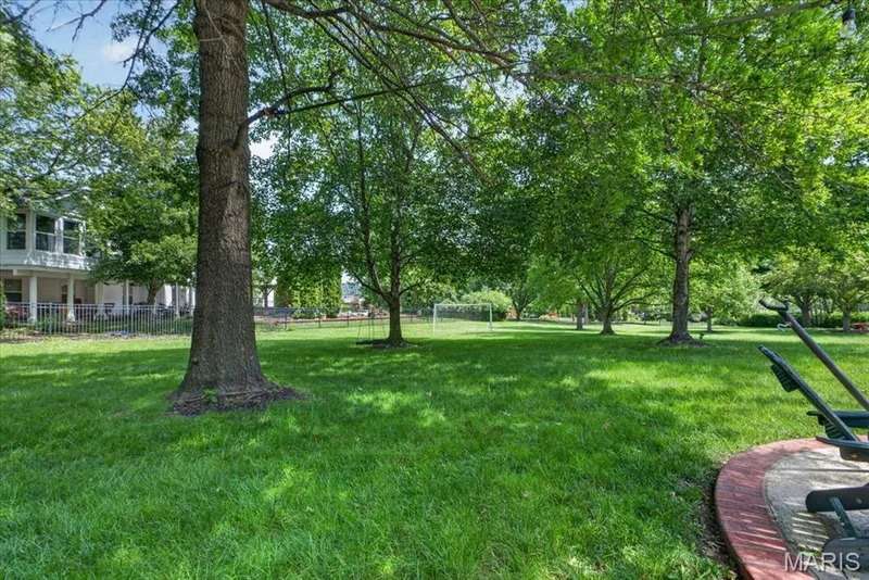 Expansive green lawn framed by mature trees, featuring a visible portion of a home with a columned porch and fencing — 17821 Wilderness Cliff Court, Wildwood, MO 63005