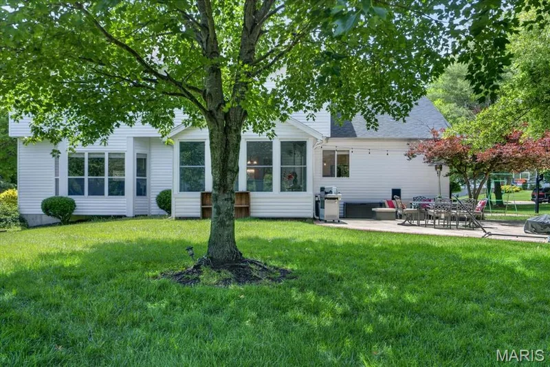 Spacious backyard featuring a large tree, vibrant green lawn, white siding, and a stone patio — 17821 Wilderness Cliff Court, Wildwood, MO 63005