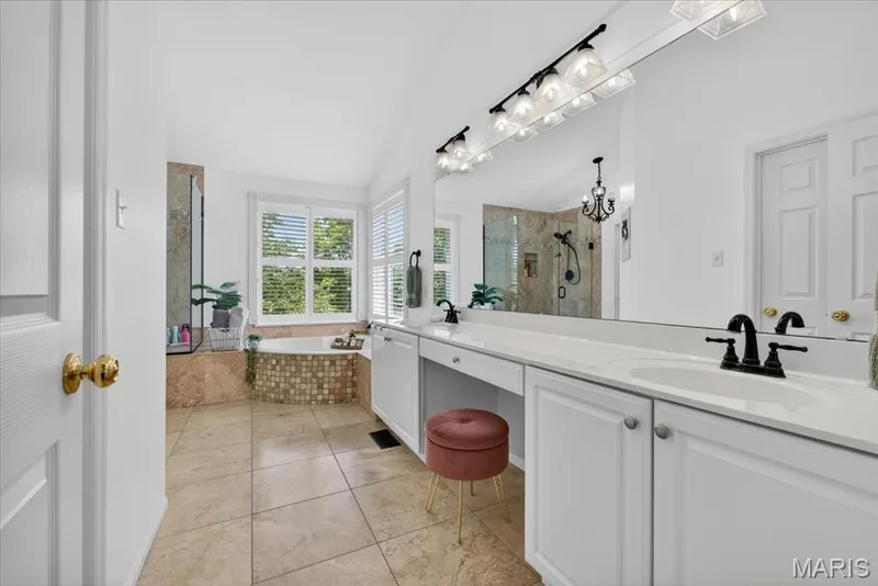 Spacious bathroom featuring a double vanity with ample counter space, a large built-in mirror, a soaking tub with mosaic tile surround, and a separate glass-enclosed shower — 17821 Wilderness Cliff Court, Wildwood, MO 63005