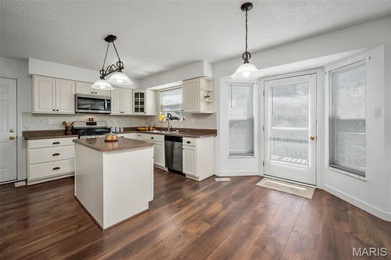 Wood-finish flooring, white cabinetry, a central island, stainless steel appliances, and a bay window with a glass-paneled door — 120 Bromley Court, O'Fallon, MO 63368