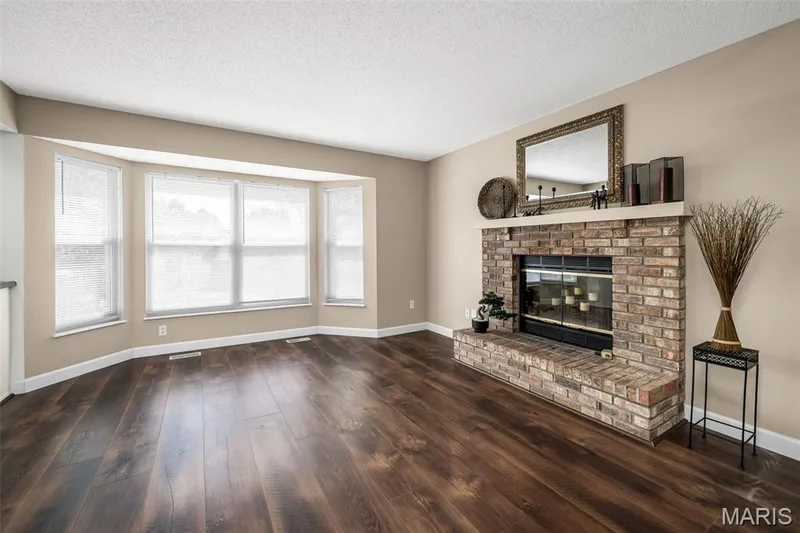Wood-finish flooring throughout, bay window with multiple panes, brick fireplace with a stone hearth, and a white mantelpiece — 120 Bromley Court, O'Fallon, MO 63368