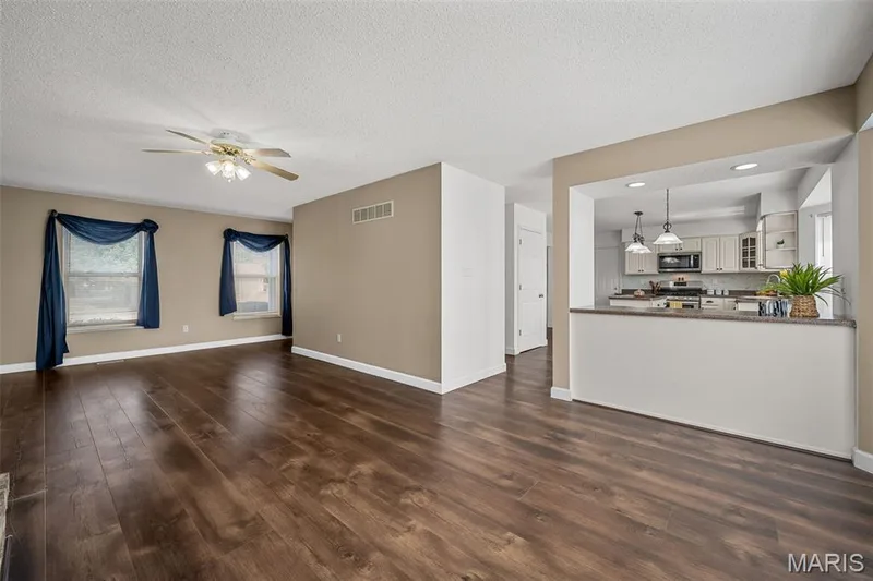 Open-concept living area showcasing rich wood-finish flooring throughout, neutral taupe walls, and abundant natural light from dual windows — 120 Bromley Court, O'Fallon, MO 63368
