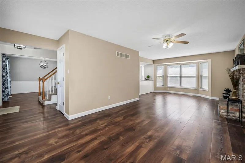 Wood-finish flooring throughout, bay windows, brick fireplace with a stone mantel, ceiling fan, and staircase with carpeted treads — 120 Bromley Court, O'Fallon, MO 63368