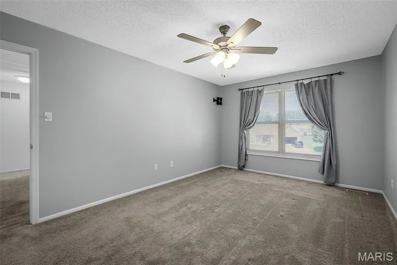 Spacious bedroom with neutral gray walls, plush carpet flooring, and abundant natural light from large multi-pane windows — 120 Bromley Court, O'Fallon, MO 63368