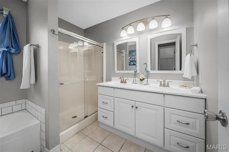 Dual vanity with white cabinetry, framed mirrors, and a multi-light fixture — 120 Bromley Court, O'Fallon, MO 63368