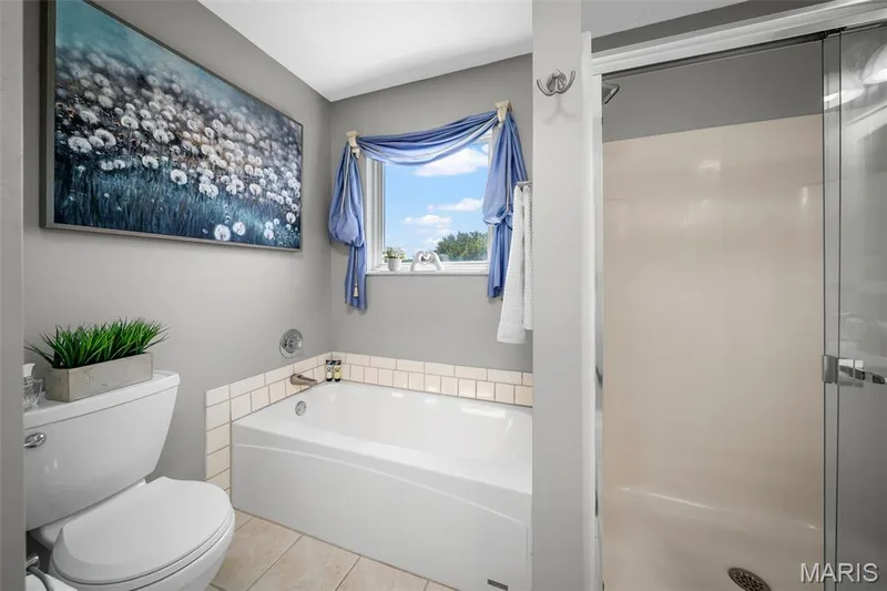 Recessed bathtub with subway tile surround, separate shower enclosure with glass door, toilet, and window — 120 Bromley Court, O'Fallon, MO 63368