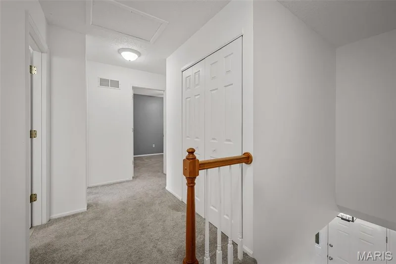 Carpeted hallway with wood banister, flush mount lighting, paneled doors, and an attic access panel — 120 Bromley Court, O'Fallon, MO 63368