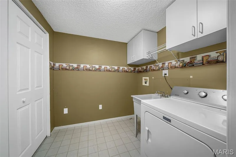 Utility room featuring white shaker-style cabinetry, a utility sink, and diamond-patterned flooring — 120 Bromley Court, O'Fallon, MO 63368