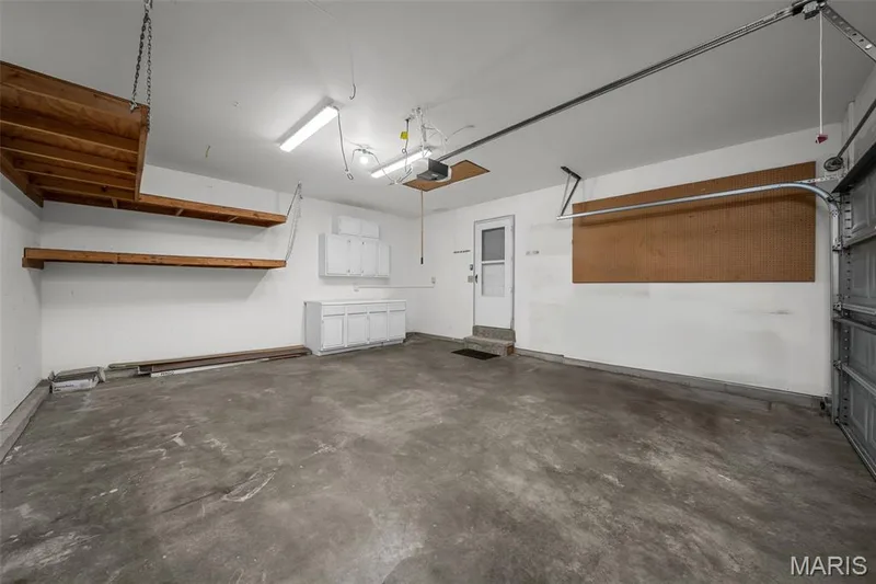 Spacious garage with concrete flooring, built-in cabinetry, and overhead shelving for storage — 120 Bromley Court, O'Fallon, MO 63368