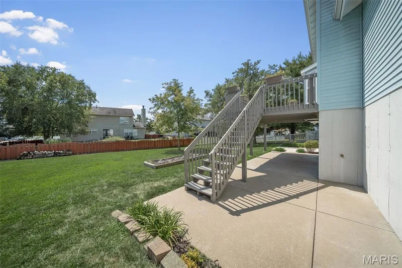Expansive rear yard featuring green lawn, a wooden privacy fence, a raised deck with stairs, and a concrete patio — 120 Bromley Court, O'Fallon, MO 63368
