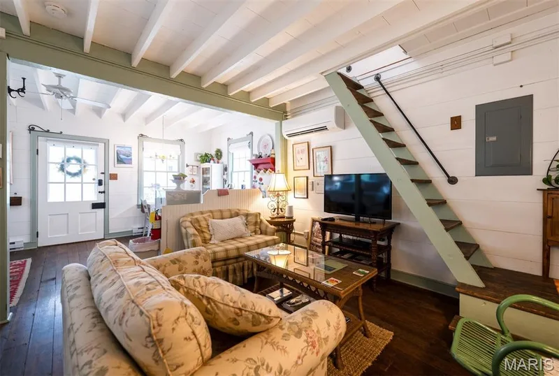 Exposed ceiling beams, wood-finish flooring, white paneling, and an interior stairway with a black metal handrail — 215 Jackson Street, Augusta, MO 63332