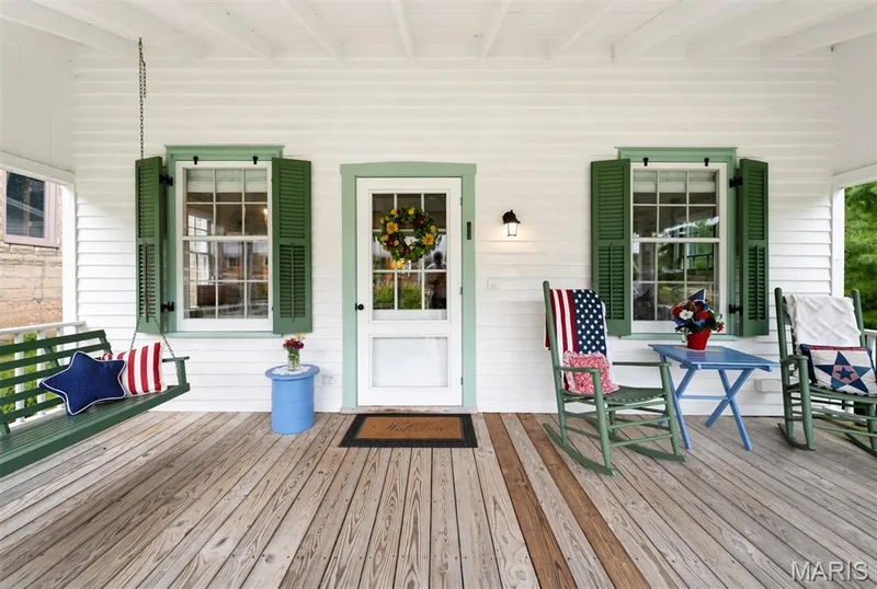 Expansive covered porch featuring wood flooring, a porch swing, and a clear glass paneled door — 215 Jackson Street, Augusta, MO 63332