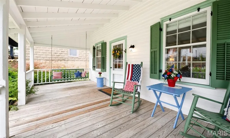 Covered front porch with wood flooring, white siding, and green louvered shutters — 215 Jackson Street, Augusta, MO 63332