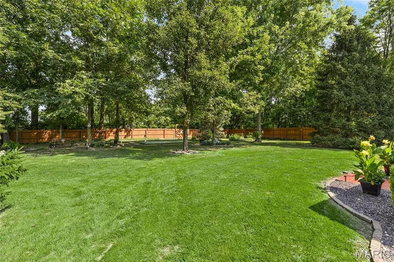 Expansive green lawn surrounded by mature trees and a wood privacy fence — 38 Fawn Valley Circle, St Peters, MO 63376