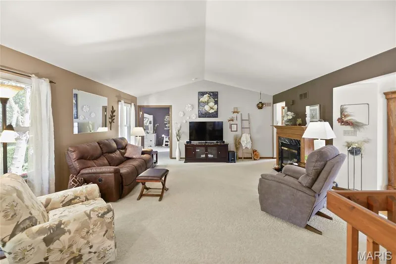 Vaulted ceiling, light-toned carpet flooring, fireplace with wood mantel, large window, and light-toned walls — 38 Fawn Valley Circle, St Peters, MO 63376
