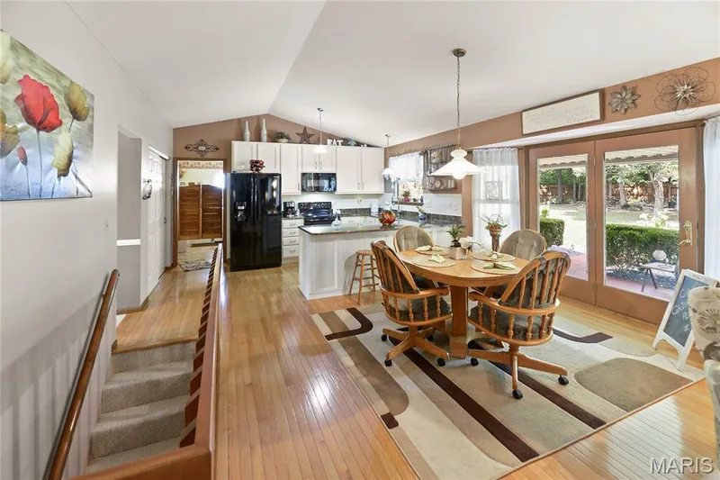 Open-concept living area with vaulted ceilings, wood-finish flooring, white cabinetry, and double glass doors opening to the exterior — 38 Fawn Valley Circle, St Peters, MO 63376