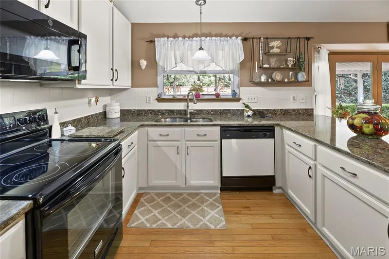 Light wood-finish flooring with white cabinetry, dark stone countertops, and a tile backsplash — 38 Fawn Valley Circle, St Peters, MO 63376