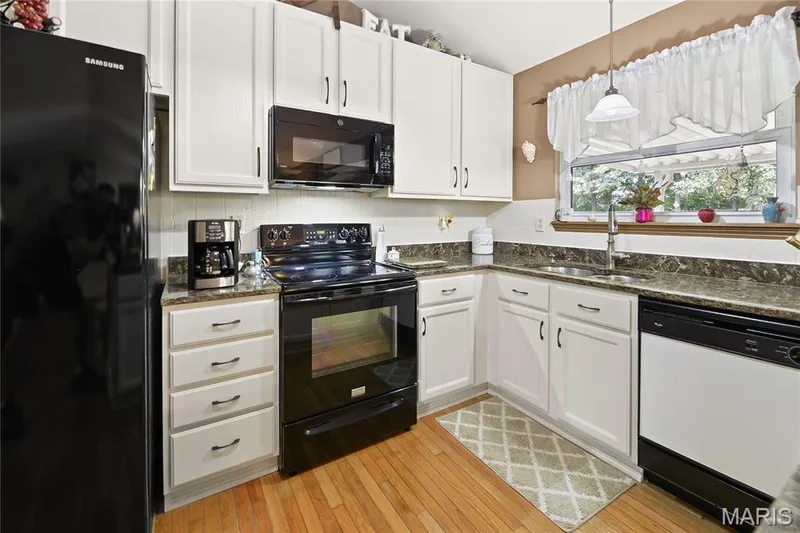 White cabinetry, wood-finish flooring, dark stone-finish countertops, black and white appliances, and a window above the sink — 38 Fawn Valley Circle, St Peters, MO 63376