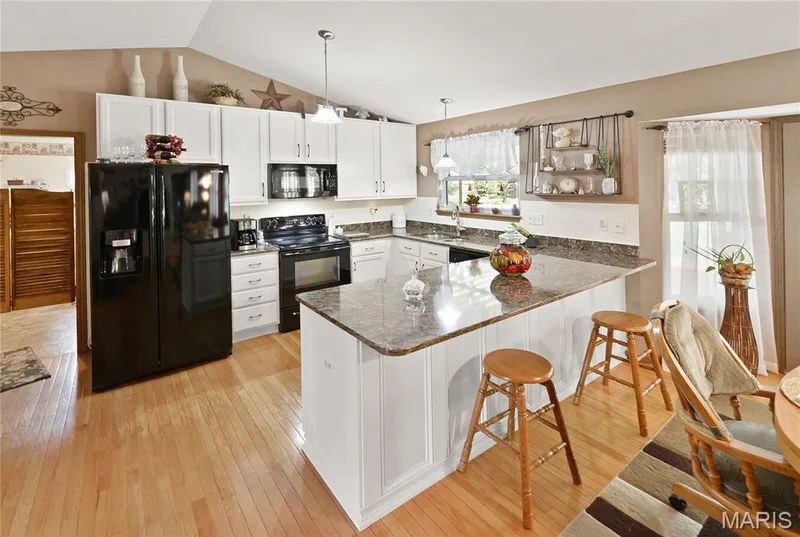 Kitchen featuring white cabinetry, black appliances, a central island with bar seating, and wood-finish flooring — 38 Fawn Valley Circle, St Peters, MO 63376