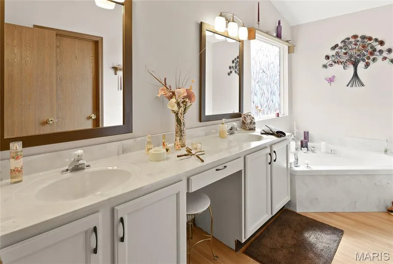 Dual vanity with integrated sinks, white cabinetry, a built-in corner tub, and wood-finish flooring — 38 Fawn Valley Circle, St Peters, MO 63376
