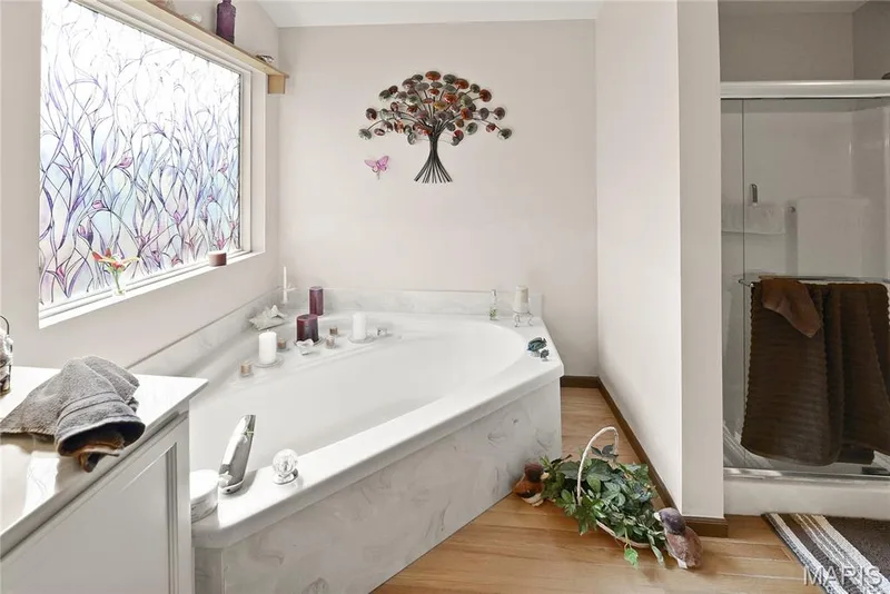 Corner soaking tub with a stone-finish surround, wood-finish flooring, and an enclosed shower — 38 Fawn Valley Circle, St Peters, MO 63376