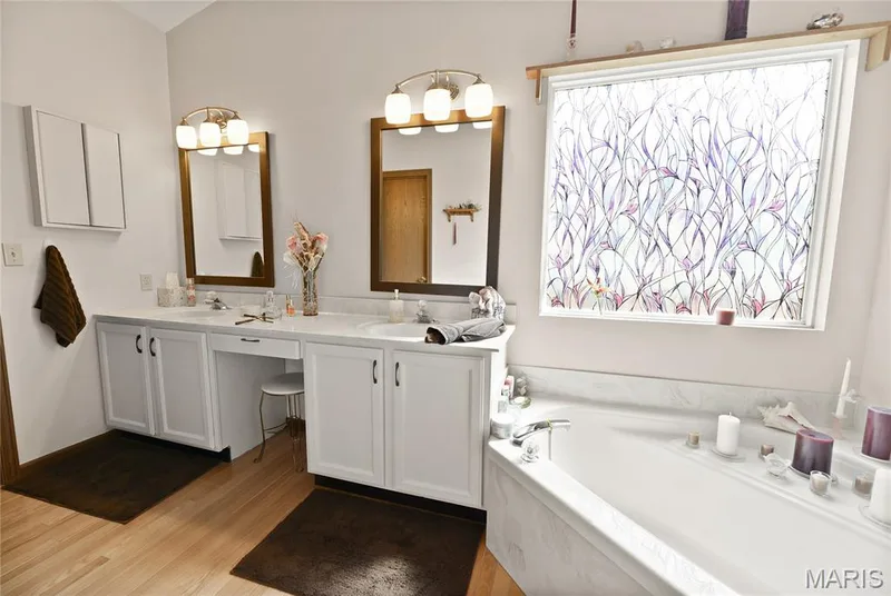 Dual vanity with undermount sinks, white cabinetry, and wood-finish flooring — 38 Fawn Valley Circle, St Peters, MO 63376