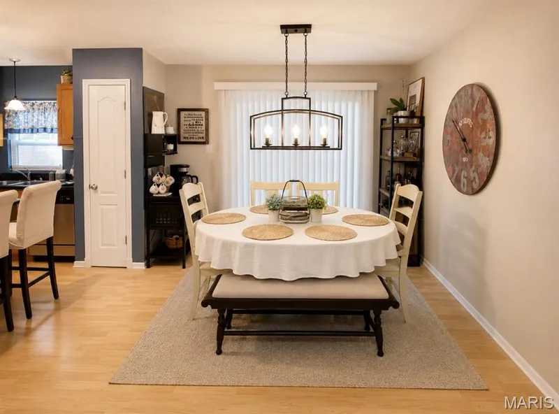 Open-concept space featuring wood-finish flooring, a contemporary chandelier, a built-in pantry, and a kitchen pass-through with bar seating — 3231 Cog Wheel Station, St Charles, MO 63301