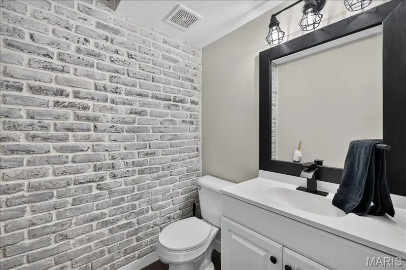 Accent brick wall, white vanity with integrated sink, black framed mirror, industrial-style vanity lighting, and matte black faucet — 53 Lions Head Court, O'Fallon, MO 63368