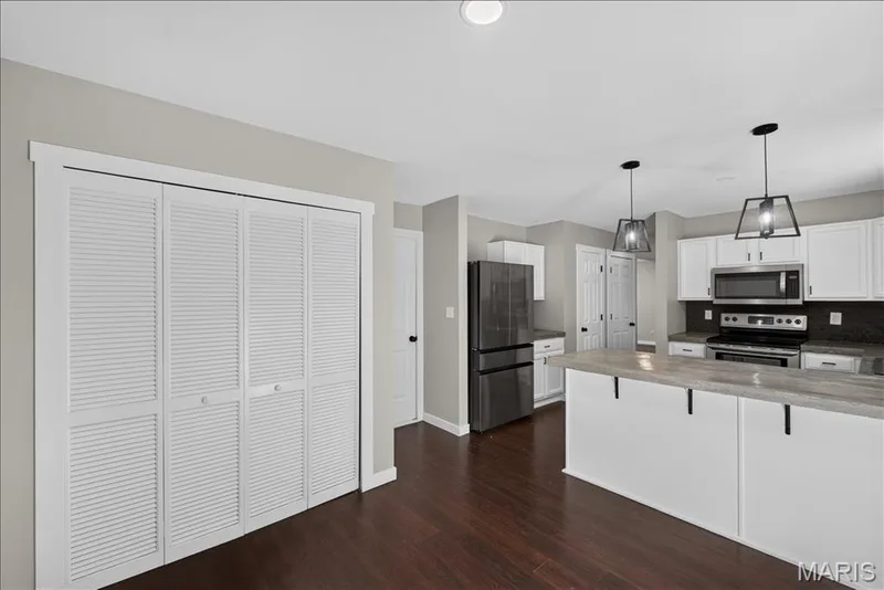 Kitchen featuring white cabinetry, stainless steel appliances, dark stone countertops, two pendant lights, and wood-finish flooring — 53 Lions Head Court, O'Fallon, MO 63368